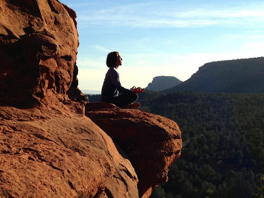 A woman meditating in a desert canyon with airy blue sky in the distance