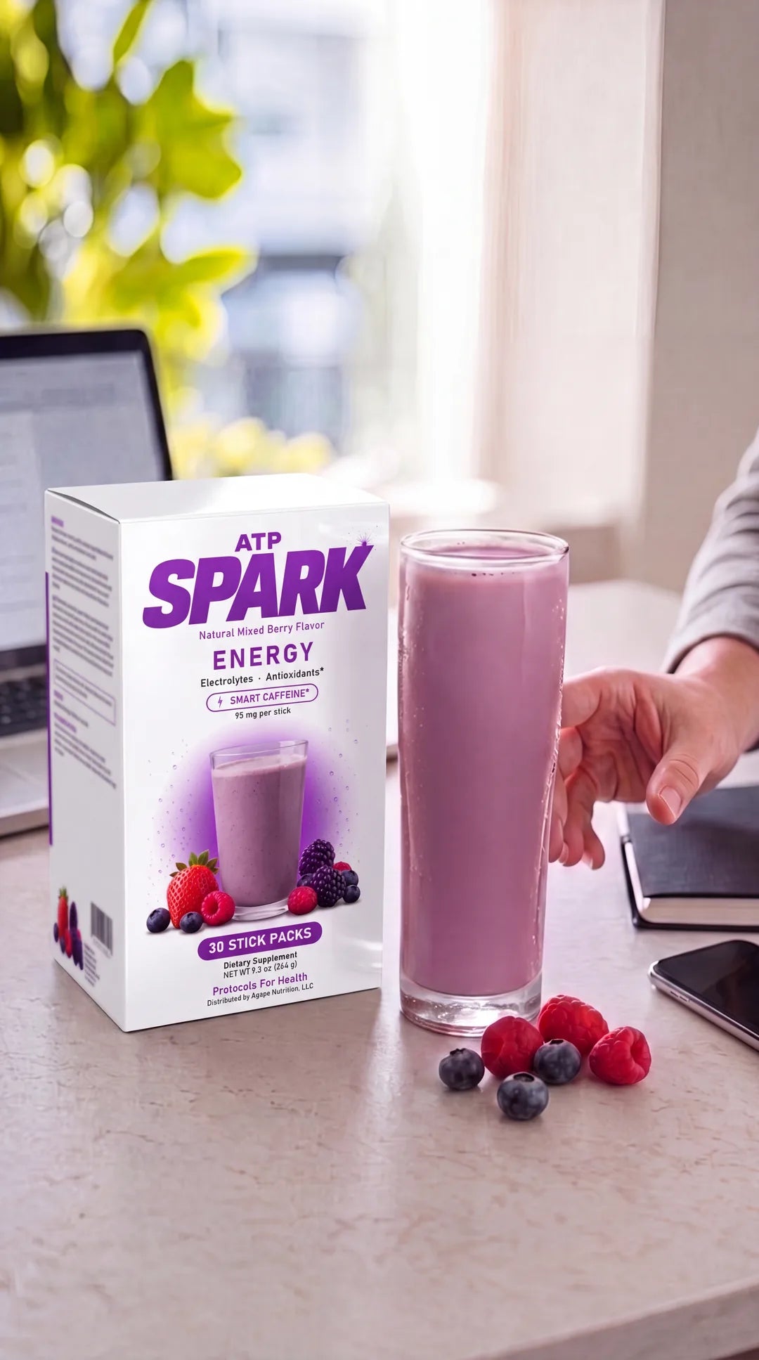 ATP SPARK box and a tall glass of deep-berry fizzing drink at a bright desk with a laptop, a hand reaching for the glass